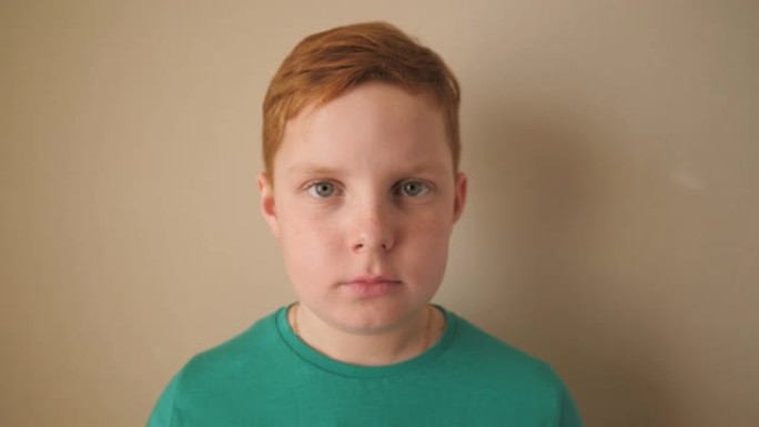 室内严肃的红头发雀斑小男孩的肖像。不高兴的小姜黄色的孩子看着里面的相机。闭上情绪的男孩与悲伤的表情在