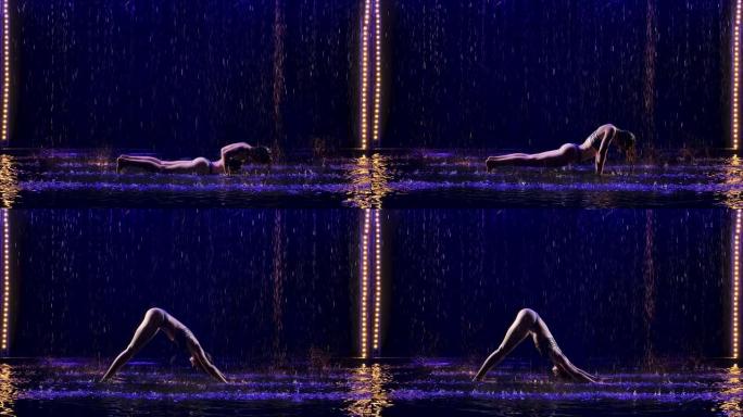 湿女人在工作室的蓝光和水雨下进行瑜伽练习。水滴中的女性身体。在黑色背景的工作室里拍摄的照片。慢动作