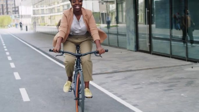 欢乐的非洲裔美国女商人沿着城市街道骑自行车