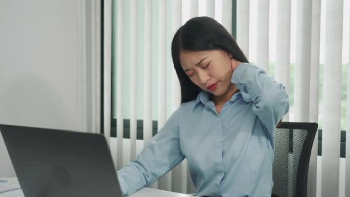年轻的亚洲妇女坐在公司办公室里，脖子疼。