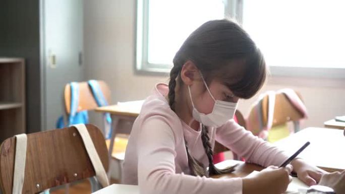 小学生在学校建筑中与老师一起在小组学习班写作。戴着口罩的小学生女孩。新型冠状病毒肺炎学校重新开放概念