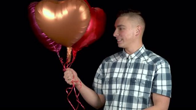 心形气球被赠送给一个年轻人。该名男子感到惊讶，将手中的氦气气球放在黑色背景上。情人节是情人的日子。