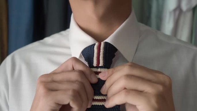 亚洲商务正装调整时尚针织领带，然后扑向镜头。背景是衣柜和套装。