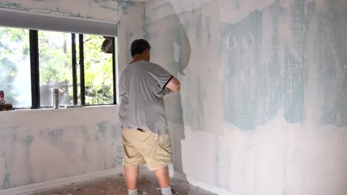 男子对准墙壁，使用抹砂刀打磨石膏板在干墙中的石膏板
