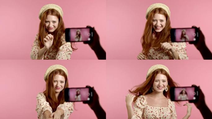 微笑的视频记录器女人在粉红色背景下录制自己在智能手机摄像头前跳舞的视频。有影响力的人制作有趣的社交媒
