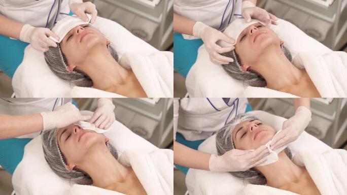 专业治疗师用白色餐巾纸清洁女性客户的脸部和颈部的特写镜头。美容和保健概念