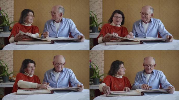 家庭，快乐快乐的老年夫妇老人和女人喜欢回忆翻阅一张家庭相册，照片坐在桌子旁