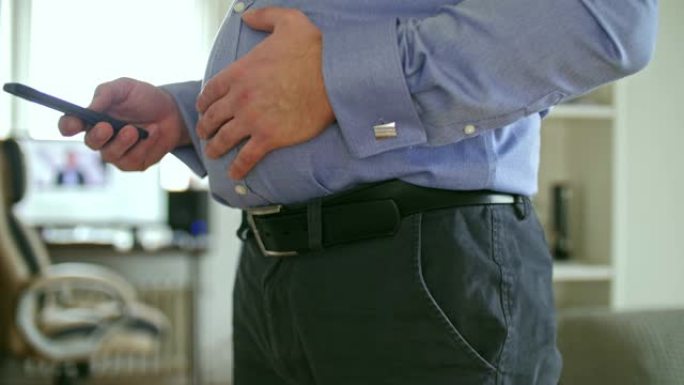 穿着衬衫的胖子抚摸腹部并使用智能手机