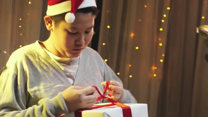 亚洲男孩戴着圣诞老人的帽子，在家准备带圣诞灯的礼品盒。