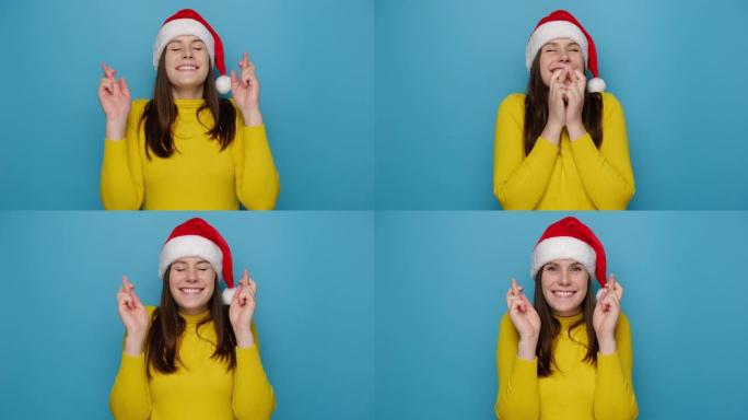 制作圣诞愿望概念。快乐可爱的年轻女子交叉手指站着，等待奇迹发生，戴着红色帽子和黄色毛衣，相信好运，孤