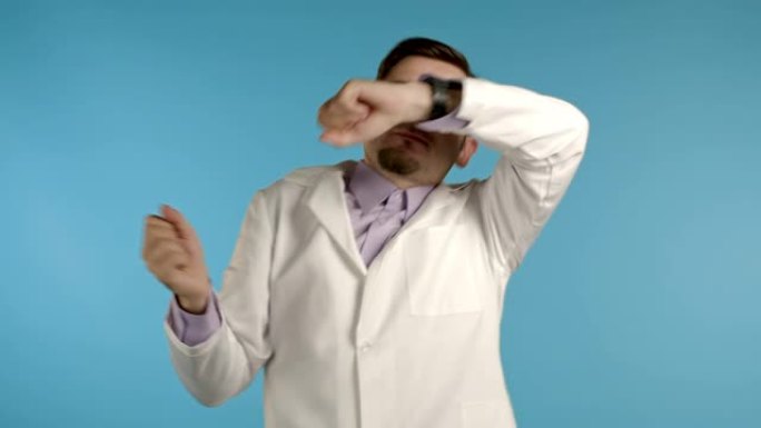 医生与胡子有趣的舞蹈，成功和运气在工作。年轻英俊的医生穿着专业的医疗白大衣被隔离在蓝色工作室背景上。