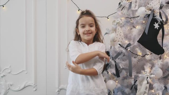 小孩子把条纹蝴蝶结放在圣诞树树枝上，看起来很满意，竖起大拇指，微笑着。