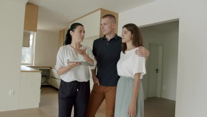 房地产经纪人在新公寓中使用数字平板电脑，并向年轻夫妇展示。