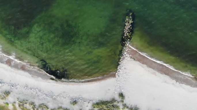 浑浊的海水拍打着白色沙滩的岸边，安装了岩壁，以防止沿海地区的动荡。海洋鸟瞰图