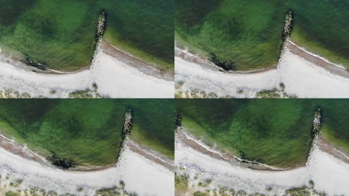 浑浊的海水拍打着白色沙滩的岸边，安装了岩壁，以防止沿海地区的动荡。海洋鸟瞰图