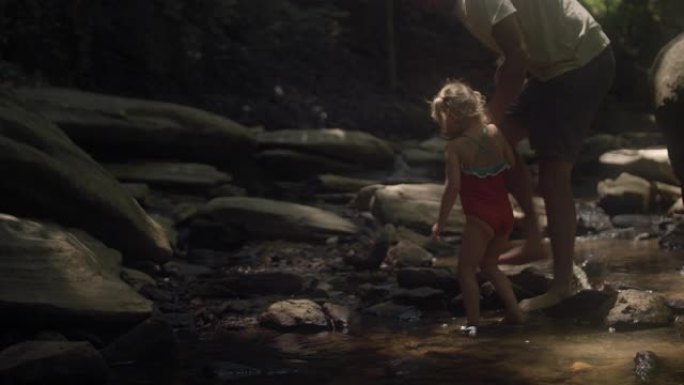 一个穿着泳衣的可爱小女孩和她的父亲走过森林中的一条小溪