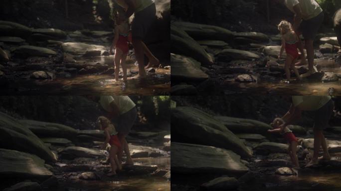 一个穿着泳衣的可爱小女孩和她的父亲走过森林中的一条小溪