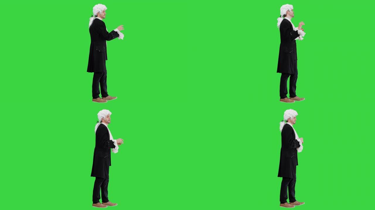 穿着老式工装外套和白色假发的男人双手在剧院里看着绿色屏幕上的相机，色度键
