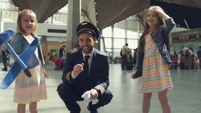 快乐的小女孩在机场航站楼从爸爸飞行员那里拿礼物，看起来开心又笑。