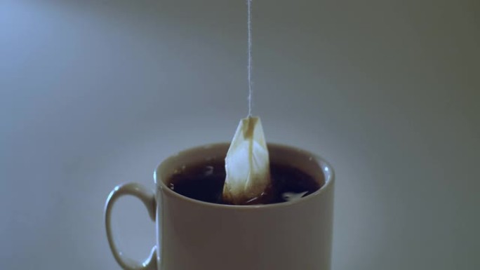 不露面的人酿造红茶，将茶袋放在室内灰色背景的白色杯子中。袋泡茶自然光慢动作复制空间文本的特写正视图。