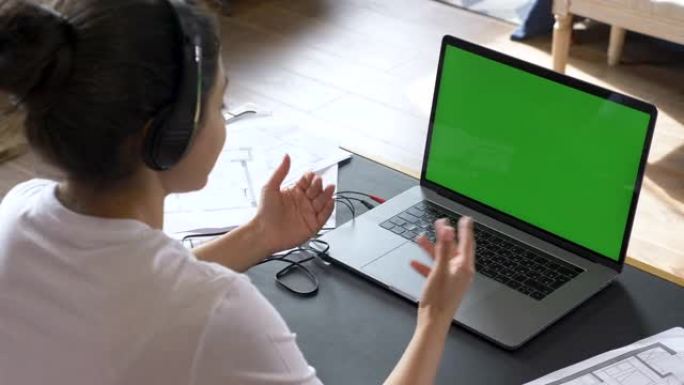 一名年轻的印度妇女举办在线会议，与人一起培训，使用带有绿屏的笔记本电脑。家里明亮的房间