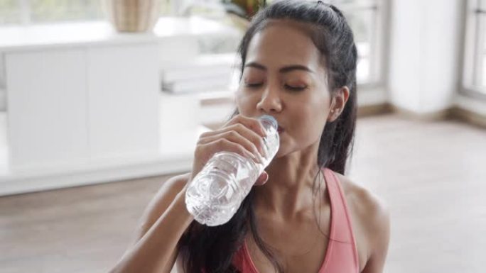 穿着运动服的迷人亚洲女性在家客厅做瑜伽锻炼后喝水。