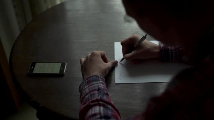 Kuchl/奥地利-2019年8月22日: 穿着格子衬衫和眼镜的男人在黑暗的房间里的木桌上写信。手机