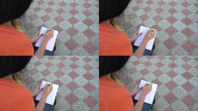 戴着医用口罩的女孩在日记中写下待办事项清单。社交远程，远程教育。学生正在公园里准备上课。一头黑发的女