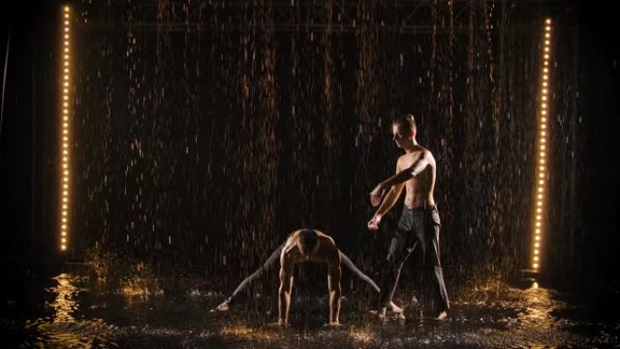 两个杂技演员在雨中表演。男人在慢动作中倒立并保持平衡