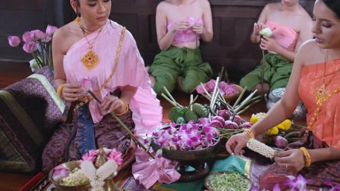 一位泰国妇女正在放莲花，另一位妇女生产花环