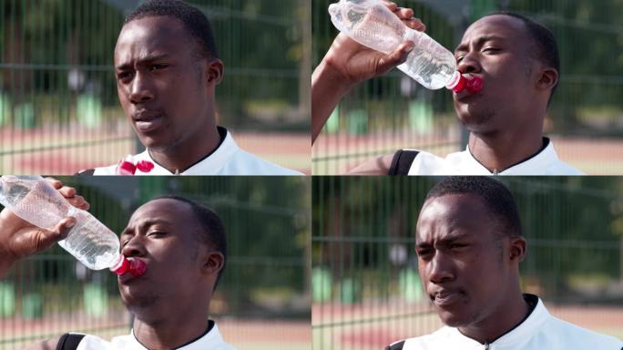 黑人篮球运动员在室外球场从瓶子里喝水，特写