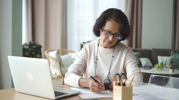 成熟的美国女商人使用笔记本电脑坐在家里的桌子上