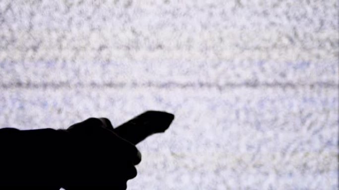 手握电视遥控器在电视屏幕背景上的轮廓，带有白色静电噪声