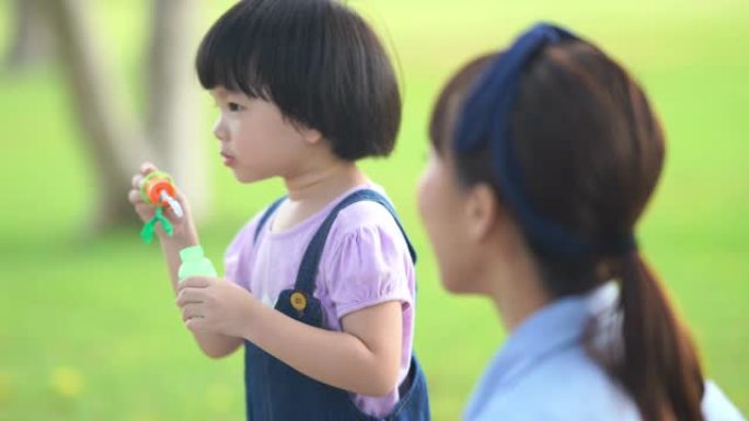 亚洲女孩在花园里和母亲玩泡泡，学龄前