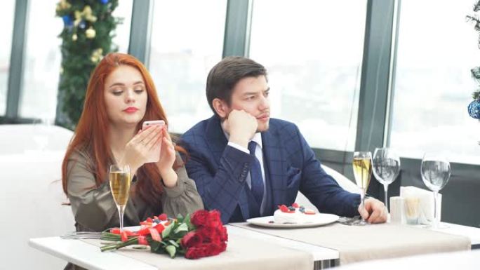 穿着燕尾服的年轻高加索男人和穿着礼服的红发女人无聊地坐在餐馆里
