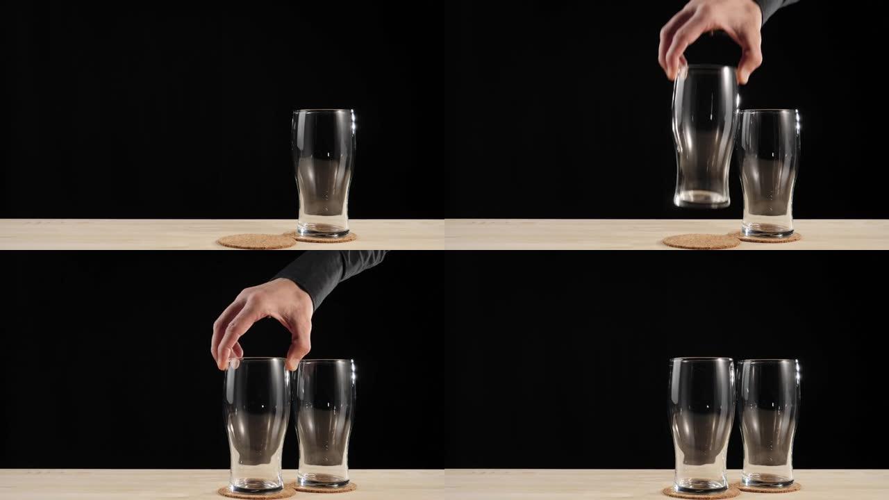 新鲜啤酒。手将第二个啤酒杯放在靠近第一个玻璃杯的啤酒杯垫上，放入黑色背景的木桌中。水滴冷新鲜啤酒。准
