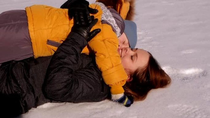 快乐的母亲，有一个年幼的儿子躺在冬季公园的雪地里拥抱。
