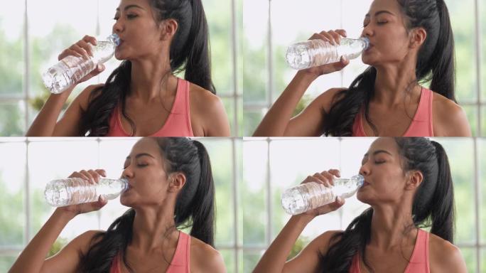 亚洲妇女在家完成瑜伽运动后喝一瓶水