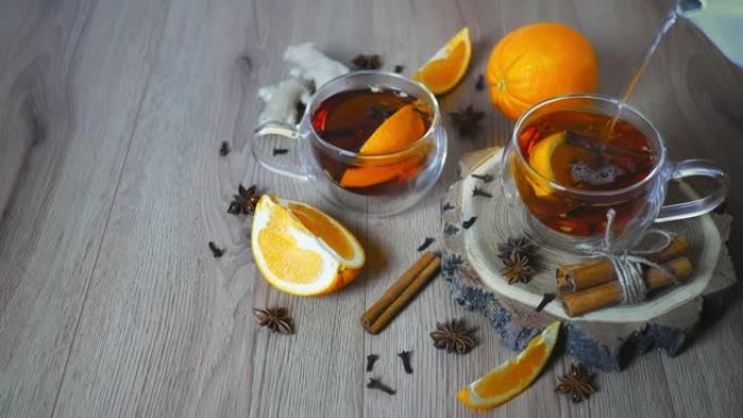 将热水倒入杯橙味茶中，将肉桂和豆蔻放在玻璃杯中，将橙子和肉桂棒放在木桌上。木质背景上的甜酒和香料。选