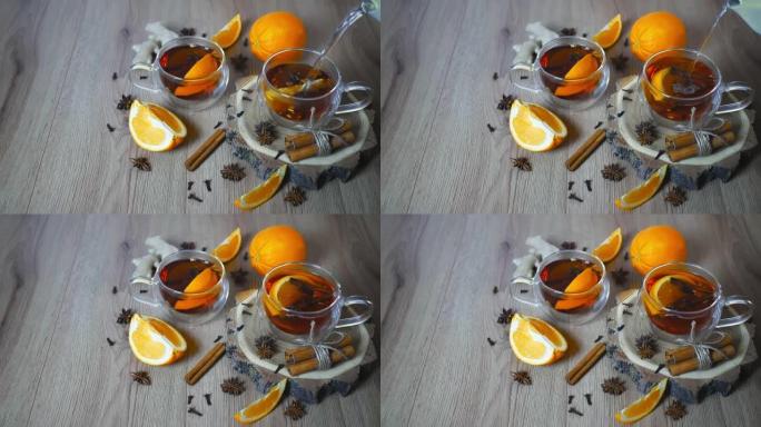 将热水倒入杯橙味茶中，将肉桂和豆蔻放在玻璃杯中，将橙子和肉桂棒放在木桌上。木质背景上的甜酒和香料。选