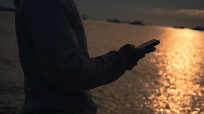 在夏天美丽的日落时，在海滩上户外运动后，休息时使用智能手机打字信息关闭运动员跑步者。