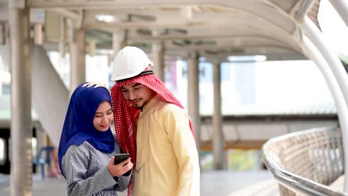 数字营销组阿拉伯人使用智能平板行走在现代穆斯林阿联酋城市触摸屏讨论。亚洲企业家在户外与老板微笑交谈