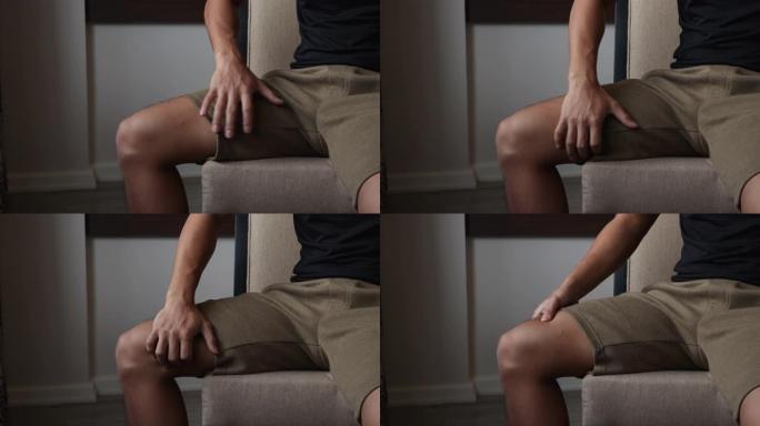 4k亚洲年轻男性做腿部大腿内侧按摩坐在椅子上，在家，大腿内侧疼痛。受伤的关节肌肉骨骼，韧带，招待治疗
