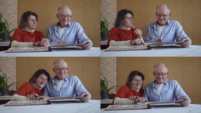 幸福的老年家庭，英俊的丈夫和妻子欢欣鼓舞，回想起过去的岁月，坐在房间的桌子旁翻阅相册