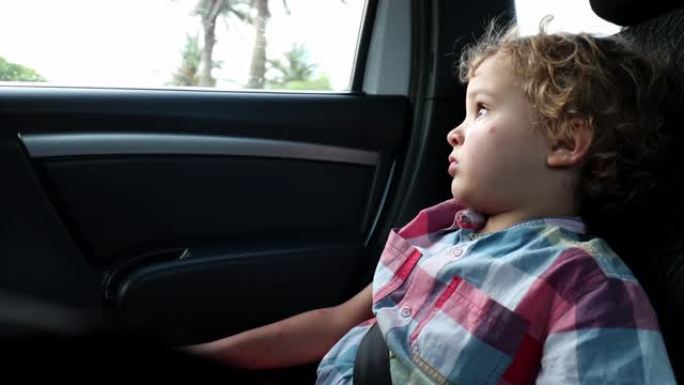 乘客蹒跚学步的男孩坐在汽车后座上，看着窗外行驶