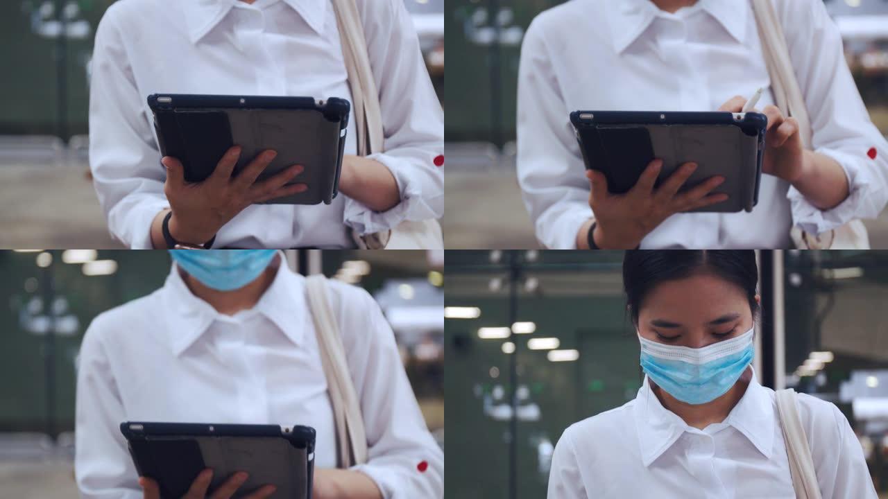 在新型冠状病毒肺炎大流行期间，女商人戴着外科口罩保护装置，并在机场候机楼坐在椅子上使用平板电脑，并保