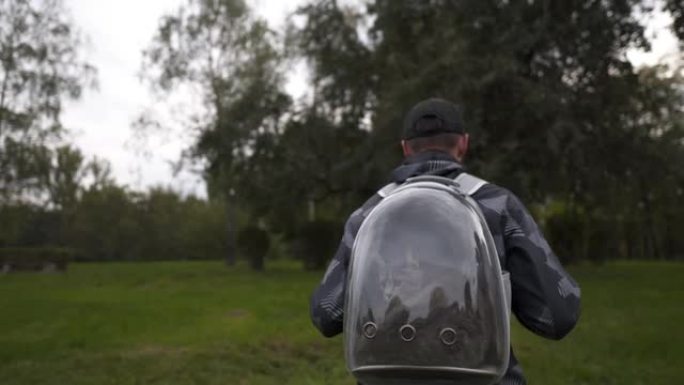 男人和猫在公园的透明背包里旅行。和宠物一起旅行。男性使用带舷窗的宠物背包。主人背着泡泡式背包的猫。旅