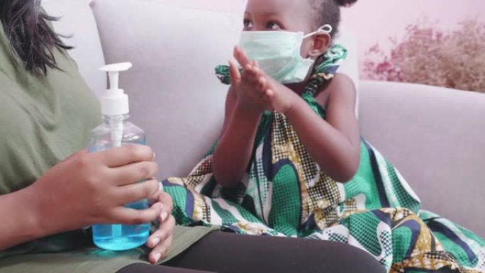 非洲妈妈照顾女儿戴口罩，并在家里的客厅用手消毒剂保护流感或新型冠状病毒肺炎疾病，妈妈和孩子戴医用口罩