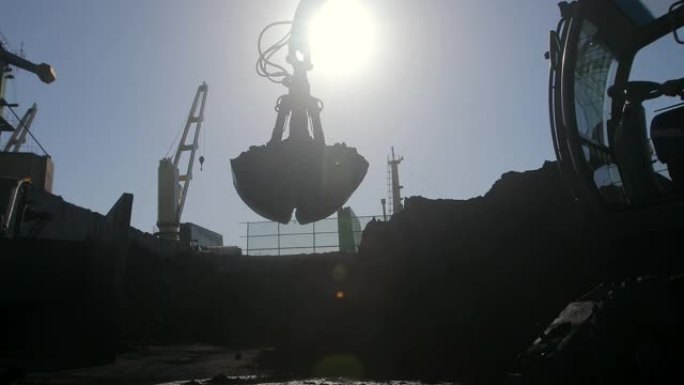 挖掘机正在将煤从大堆中装载到输送机上。船舶上人类煤的装载。
