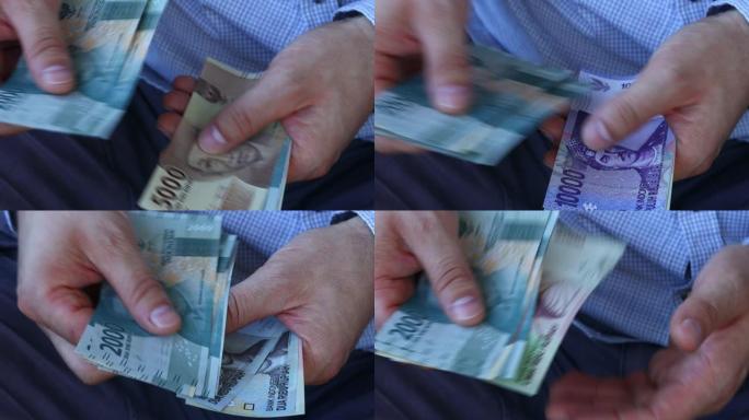 一个穿着商务衬衫的人数着印尼盾的钱。各种钞票